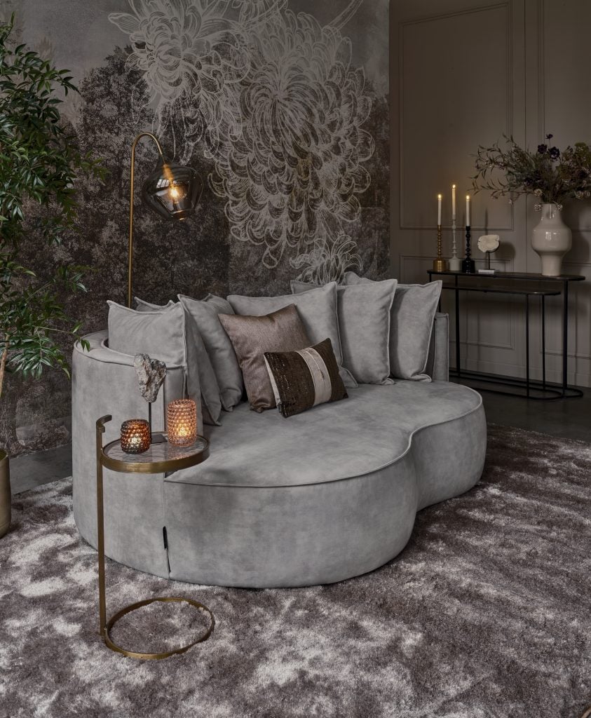 Lounge sofa with organic shapes and matching back cushions in a gray velvet fabric, and gold and bronze accessories.