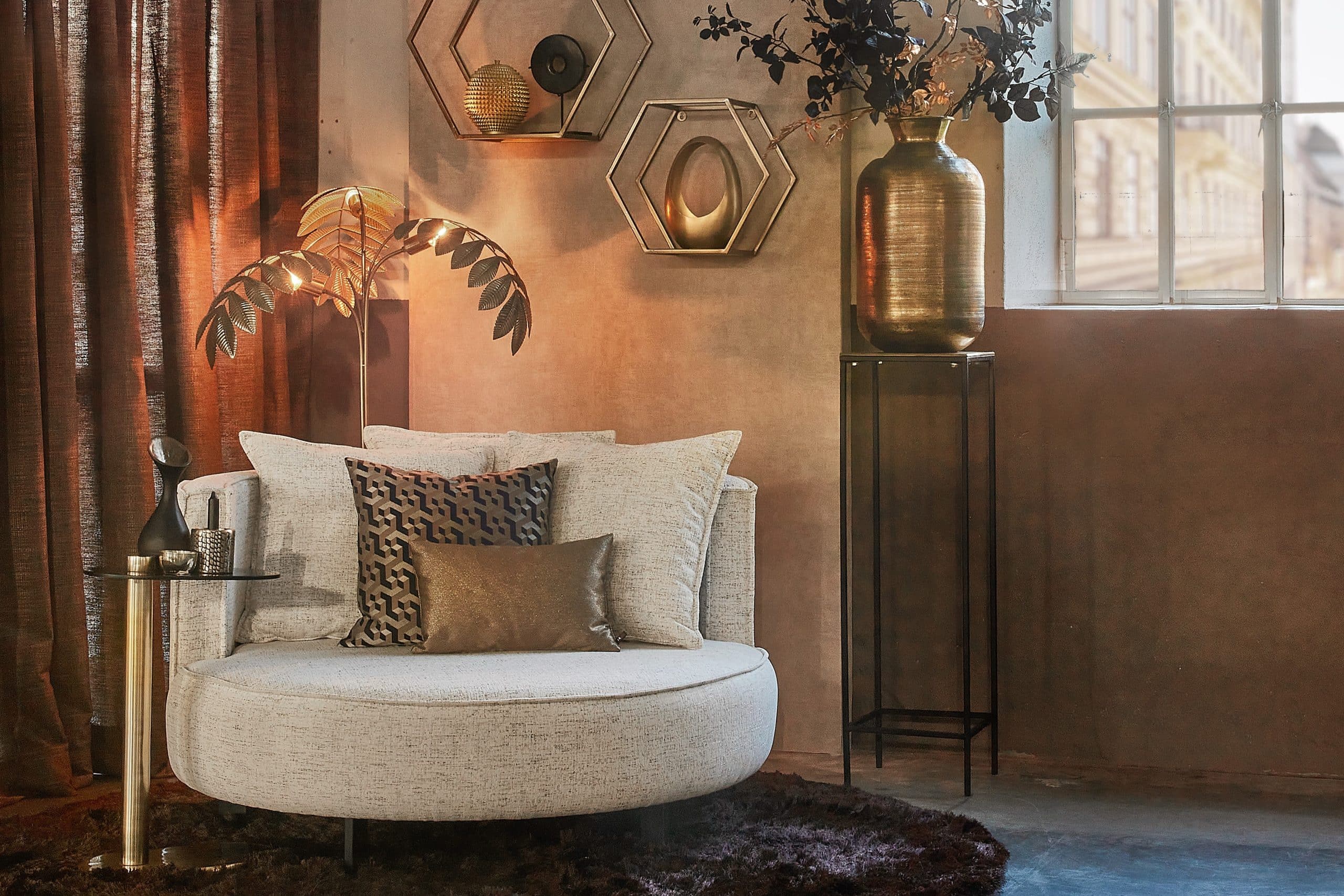 Ronde loveseat adele in een lichte beige stof. met sfeervolle accessoires in bruin en goud.